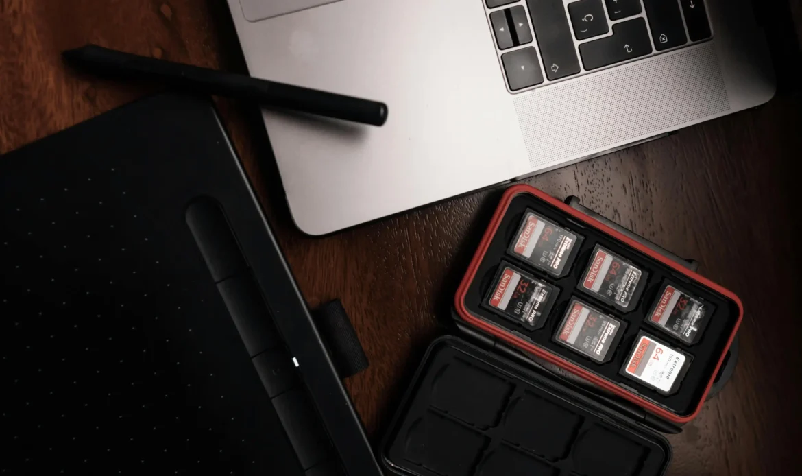 A Notebook, Laptop, and SD Card Case Sit Next to Each Other on the Desk of an EnforceMG Employee.